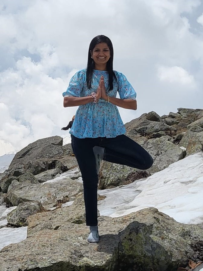 Yoga Instructor in a yoga pose standing on one leg on a rock with snowy mountains in the background.