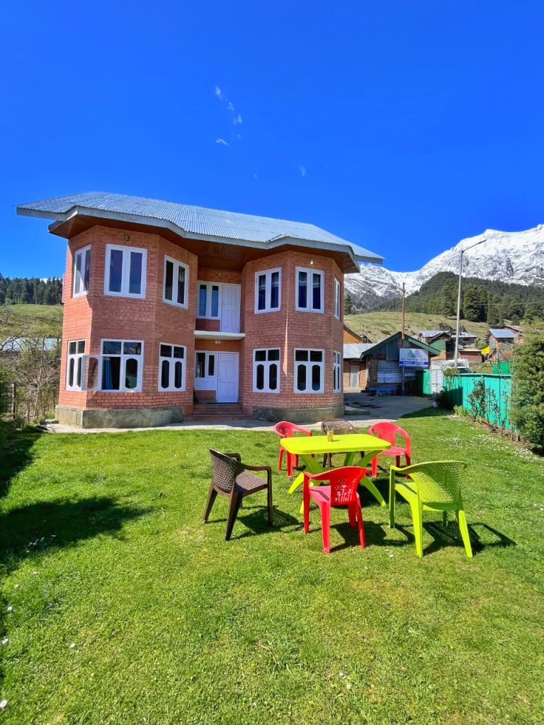 Image of the stay at the Aru Valley in Kashmir on a bright sunny day with red and yellow chairs on green grass.